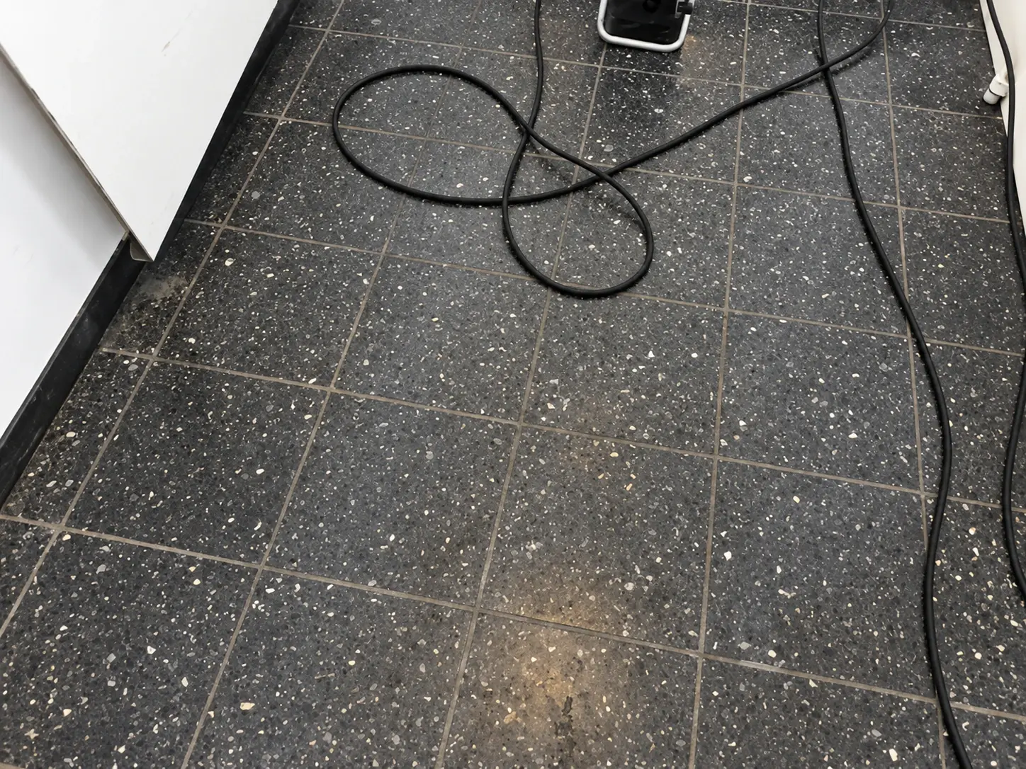 Dunkler Fliesenboden vor der Reinigung mit Gerät und Kabel